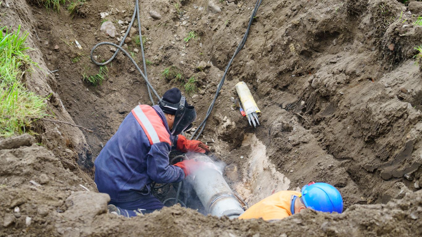 Workers performing underground pipe work in trench, showcasing residential sewer mainline repairs.